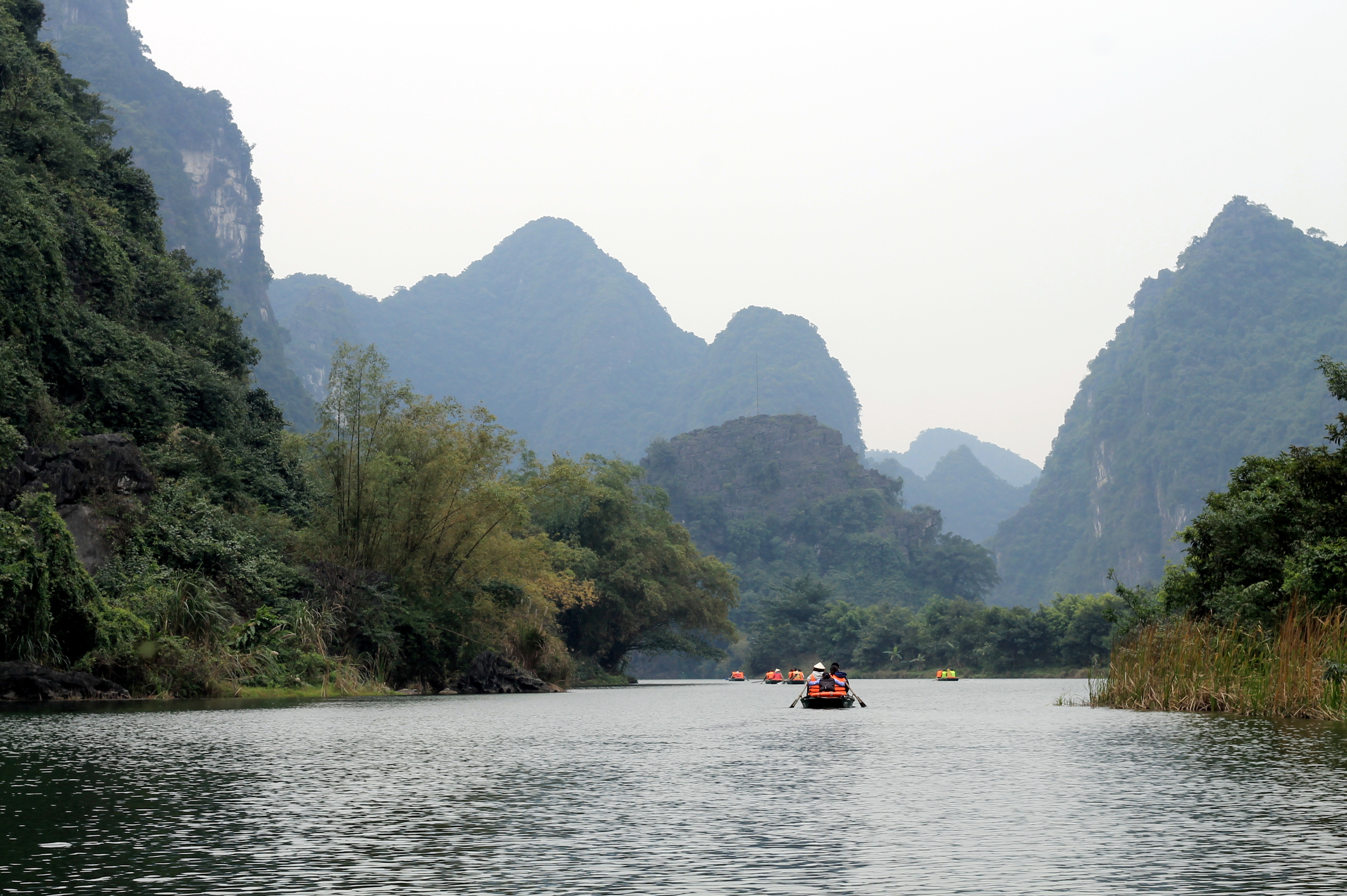 Rowboat passing through a cave beside green limestone karst scenery near Ninh Binh in Vietnam